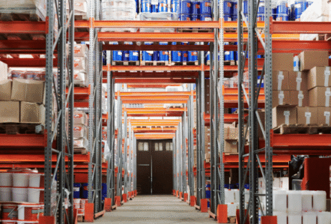 Aleja w magazynie wysokiego składowania pełna regałów z paletami i towarami, ilustrująca środowisko pracy omawiane w przewodniku "Angielski w logistyce"
