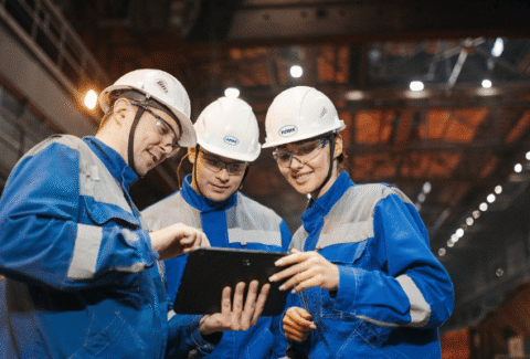 Zespół inżynierów w kaskach ochronnych analizujący dane na tablecie w hali produkcyjnej, symbolizujący profesjonalną komunikację i dojrzałość systemu IATF 16949.
