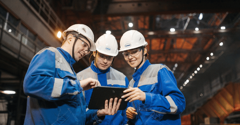 Zespół inżynierów w kaskach ochronnych analizujący dane na tablecie w hali produkcyjnej, symbolizujący profesjonalną komunikację i dojrzałość systemu IATF 16949.